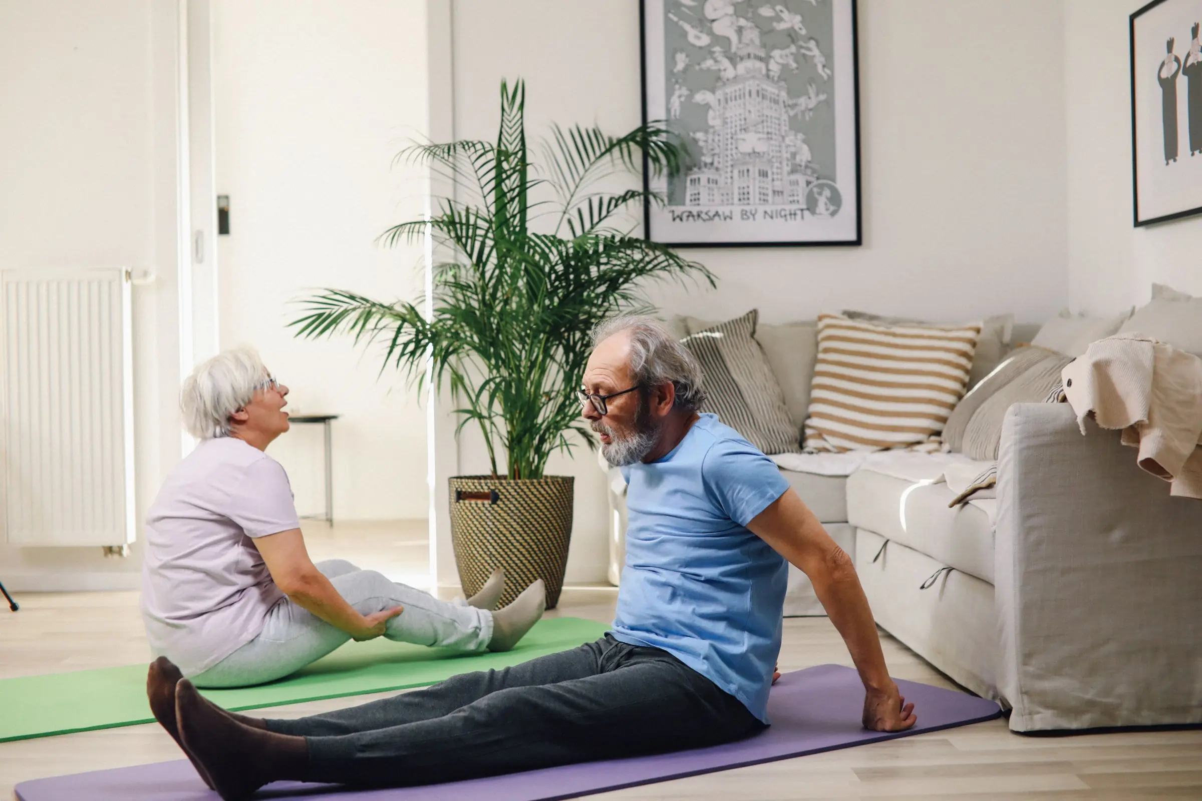 An older couple doing seated stretching exercises on mats in their living room