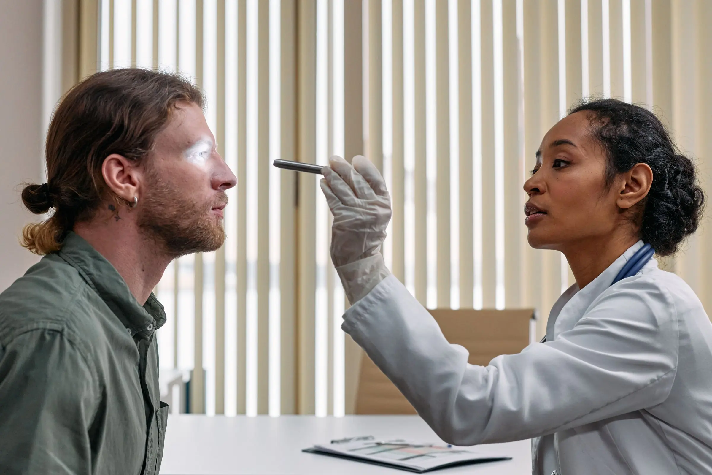 A clinician shining a small light towards a man's eyes during an examination