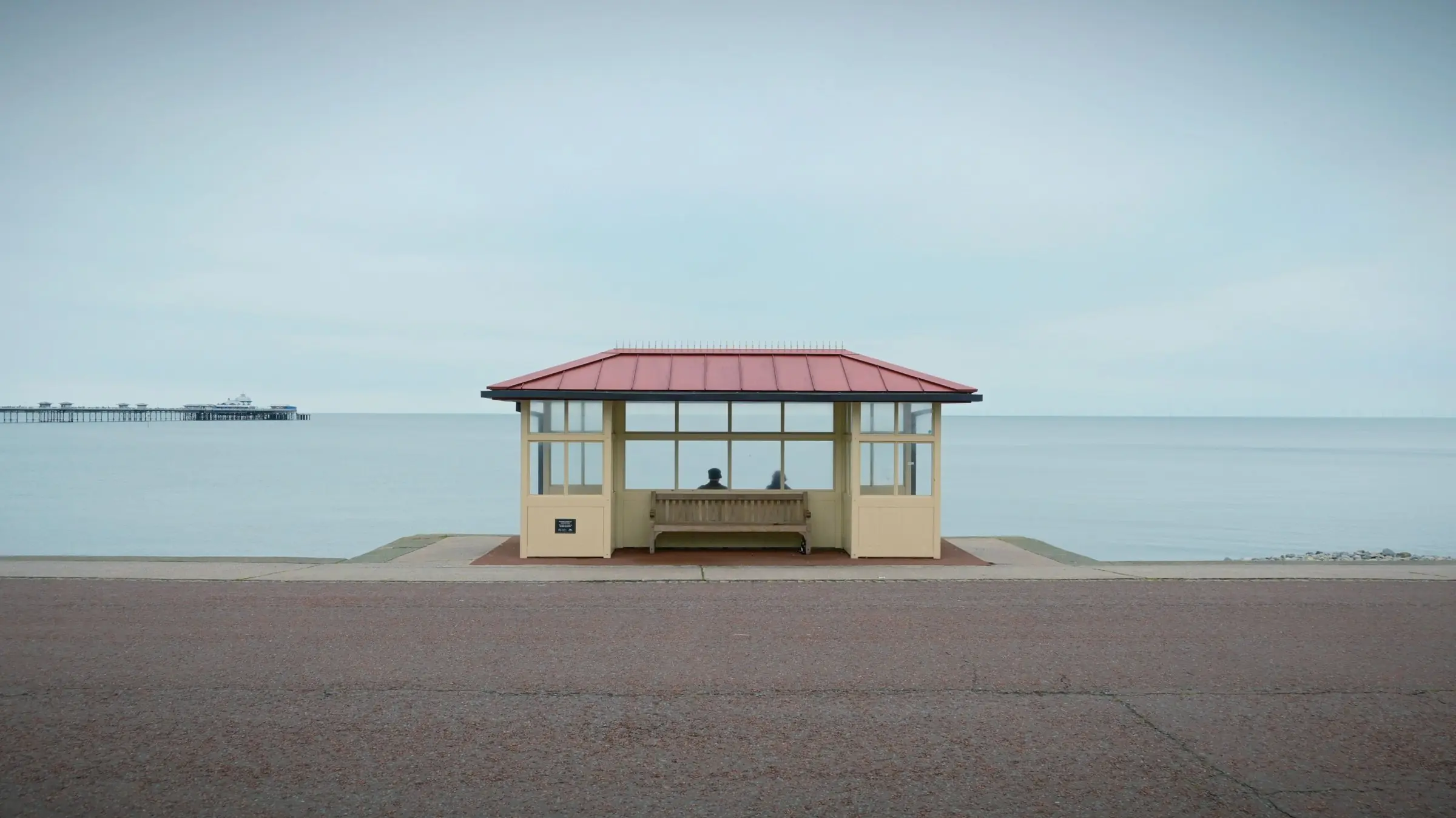 A seafront shelter with a red tiled roof on an empty promenade, looking out to a calm sea