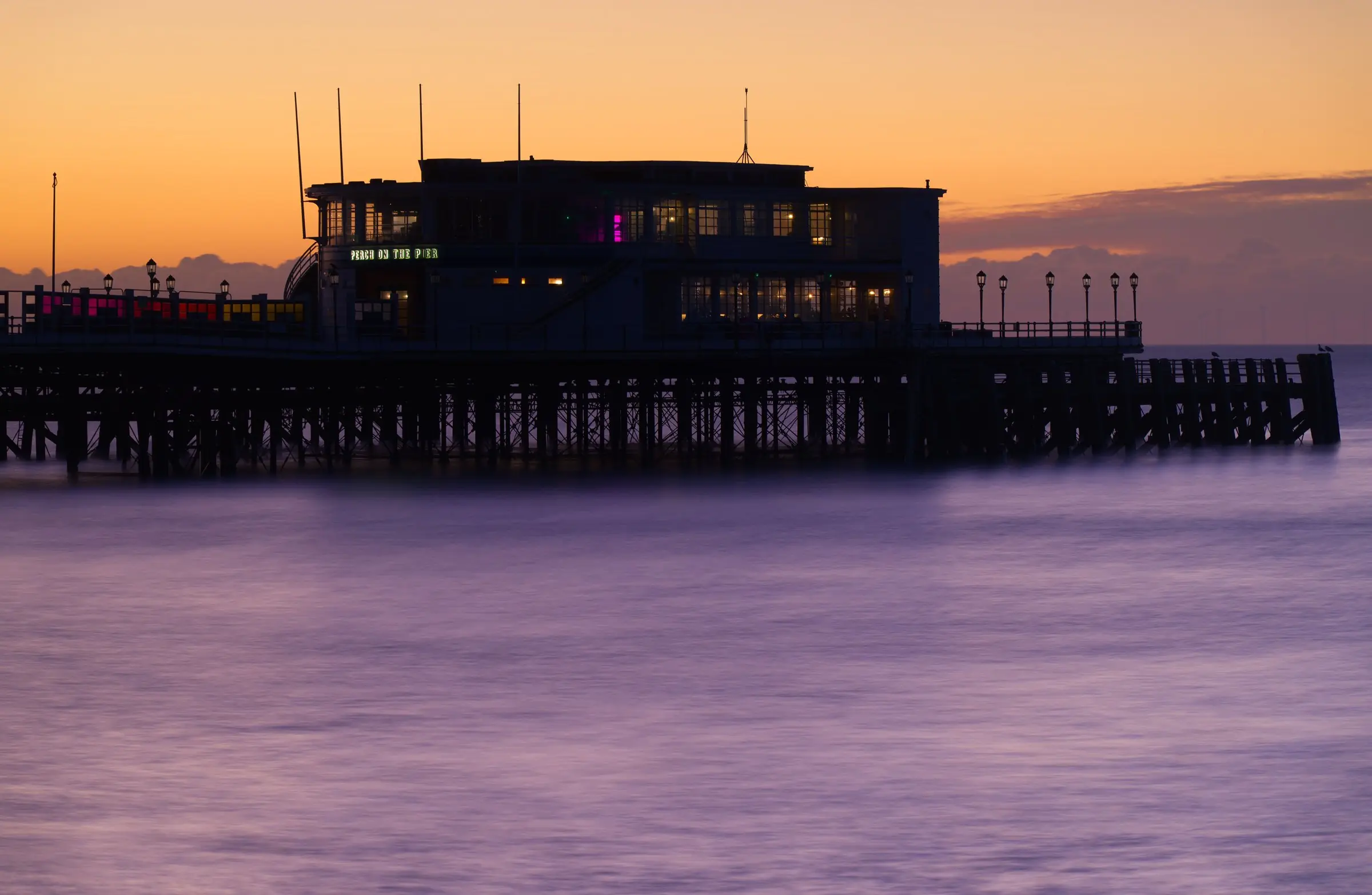 Worthing Pier at sunset, with a calm sea and a pink and orange sky